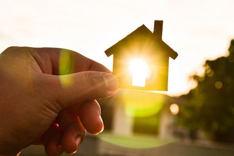 A hand holds a cutout of a house in front of the sun.