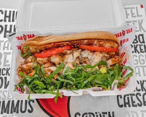 Sub sandwich with chicken, tomato, lettuce, and cheese in a takeout container.