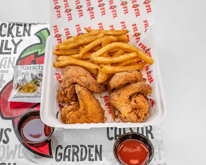 Fried chicken wings, fries, and sauces in a white container on a branded background.