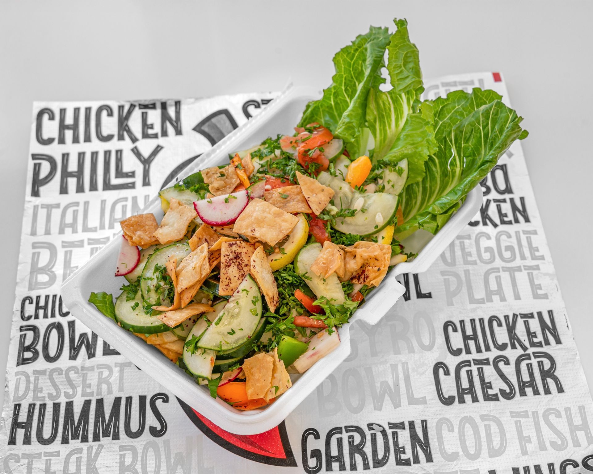 A bowl of salad with croutons , tomatoes and basil on a wooden table.