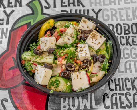 Greek salad with feta cheese, cucumbers, olives, and vegetables in a black bowl.