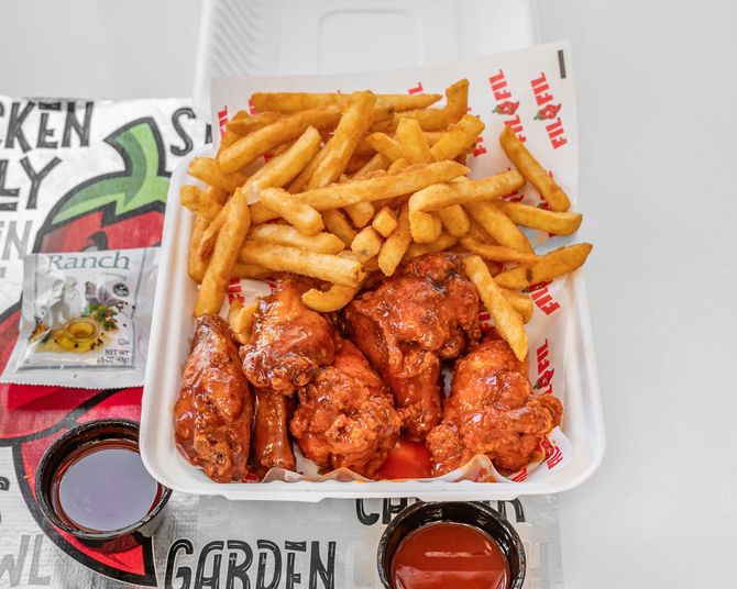 Chicken wings with fries, ranch, and two sauces in a takeout container.