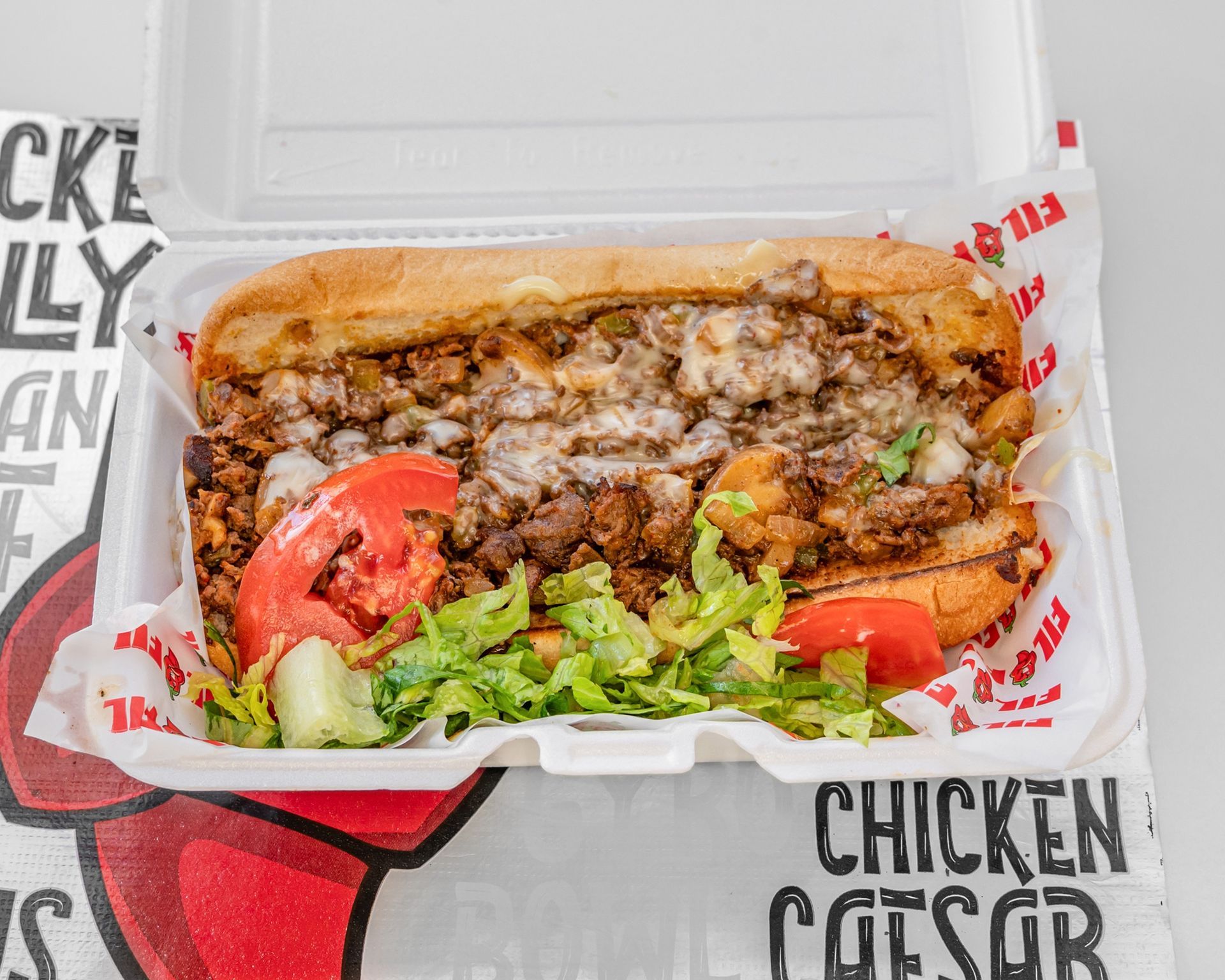 A sub sandwich with meat , lettuce , tomatoes and cheese on a wooden table.
