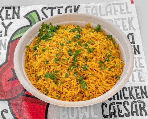 Yellow rice with parsley in a white bowl, on a table with printed text.