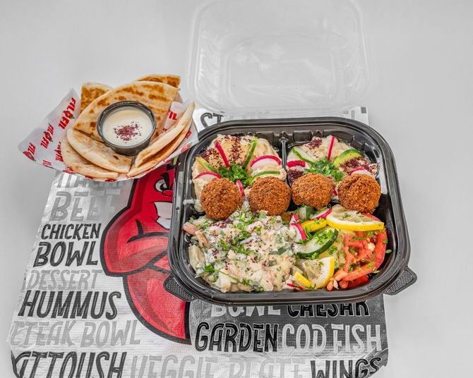 Mediterranean platter with falafel, hummus, salad, pita, and dip on a branded paper.