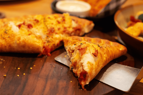Close-up of a slice of stuffed crust pizza on a wooden surface. A pizza cutter is under the slice.