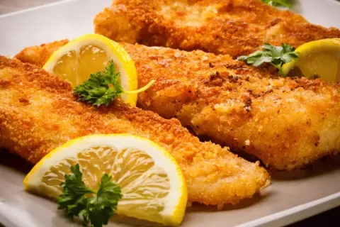 Fried fish fillets with lemon slices and parsley on a white plate.