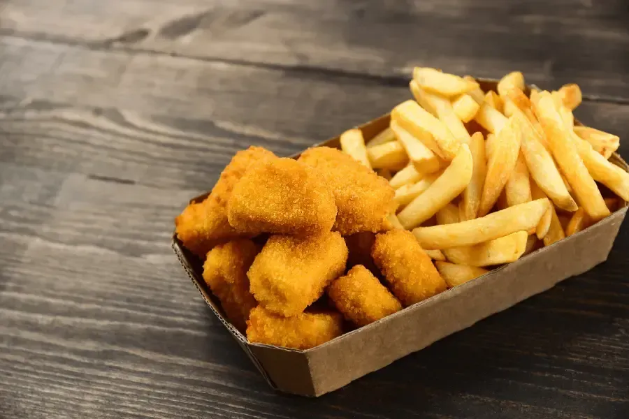 Chicken nuggets and french fries in a cardboard tray on a wooden surface.