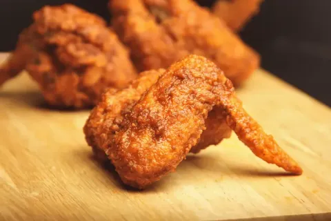 Crispy fried chicken wings on a wooden board, close-up shot.