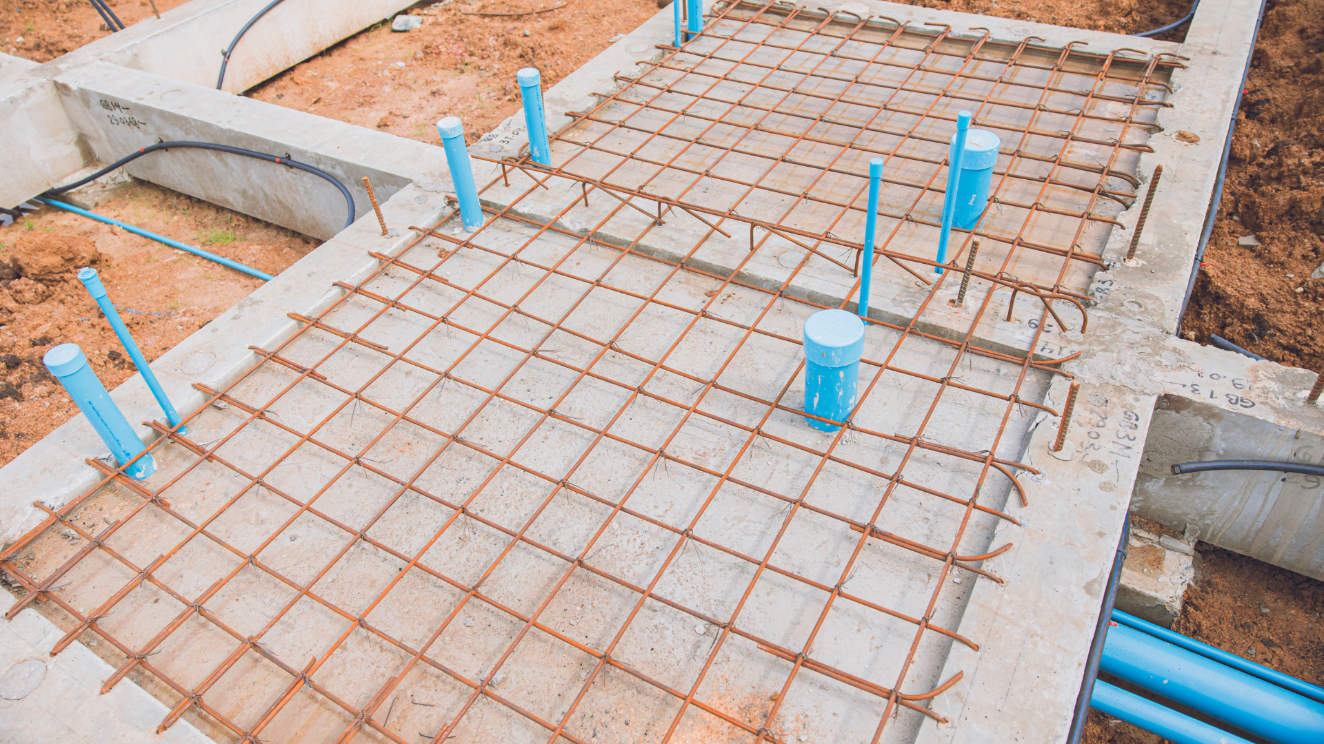 Concrete foundation under construction with rebar grid and blue plumbing.