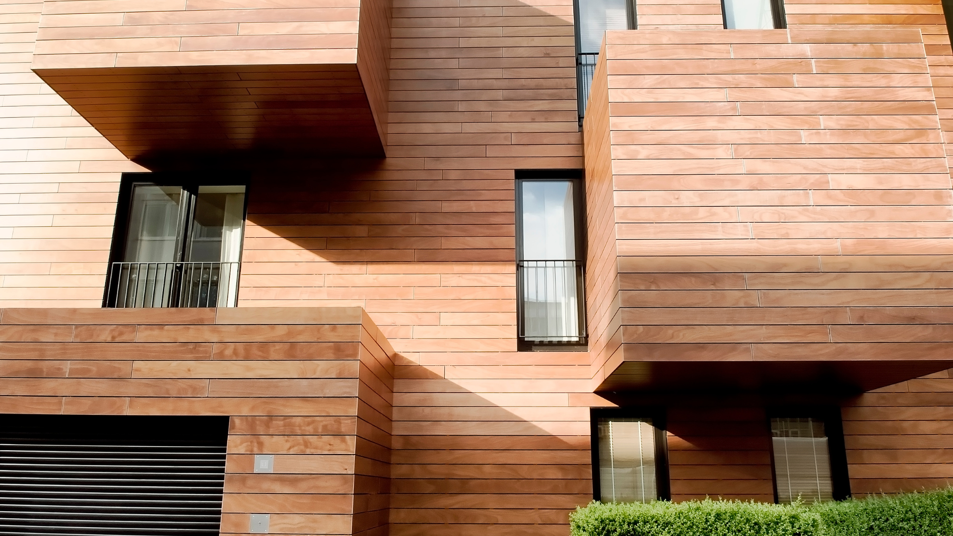 Modern building with stacked rectangular elements, brown horizontal stone, small windows, and black garage door.