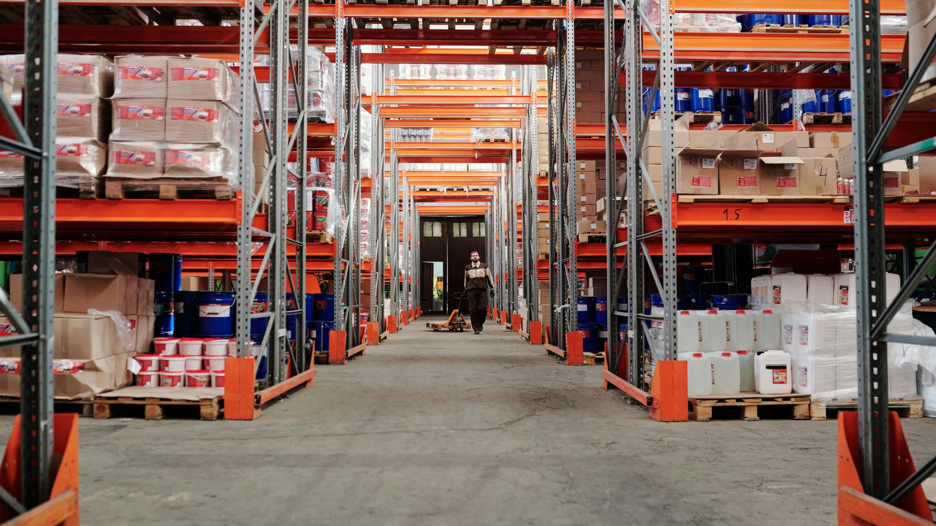 Warehouse aisle lined with orange shelving and pallets loaded with goods.