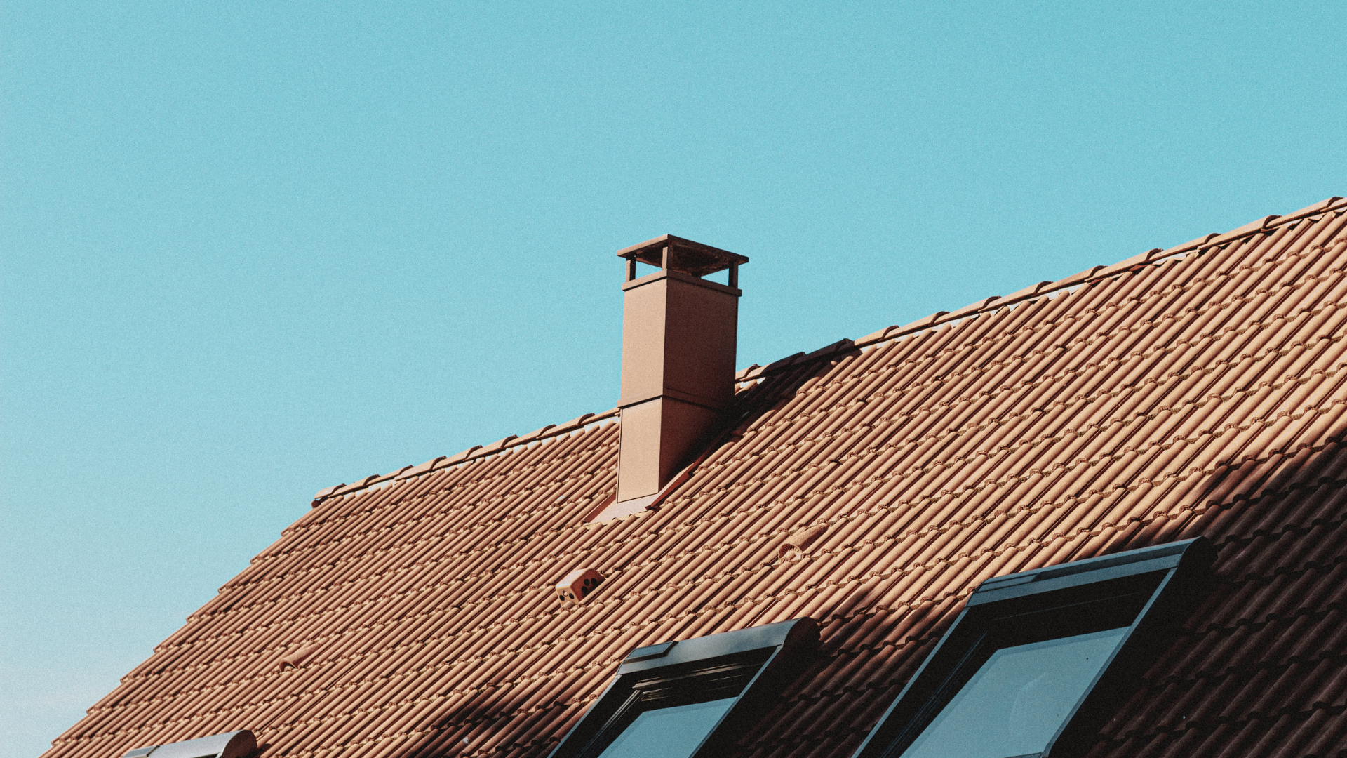 Red tiled roof with chimney against a clear blue sky.
