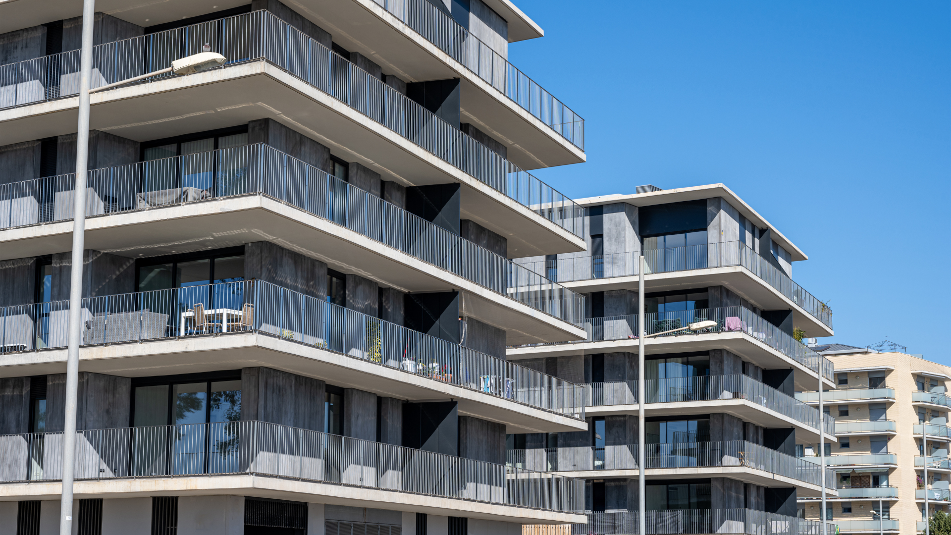 Modern apartment buildings with gray facades and balconies against a blue sky.
