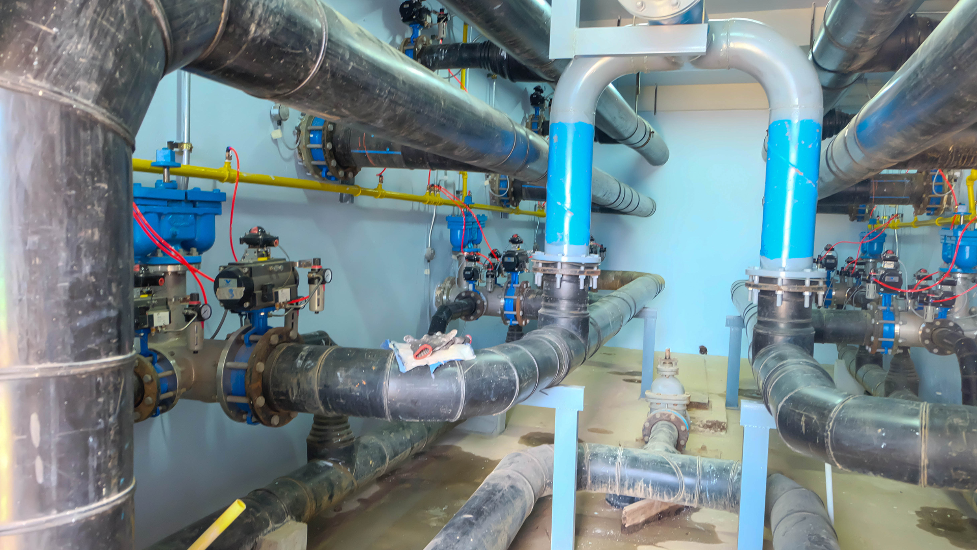 Complex network of black and blue pipes, valves, and fittings in an industrial setting.