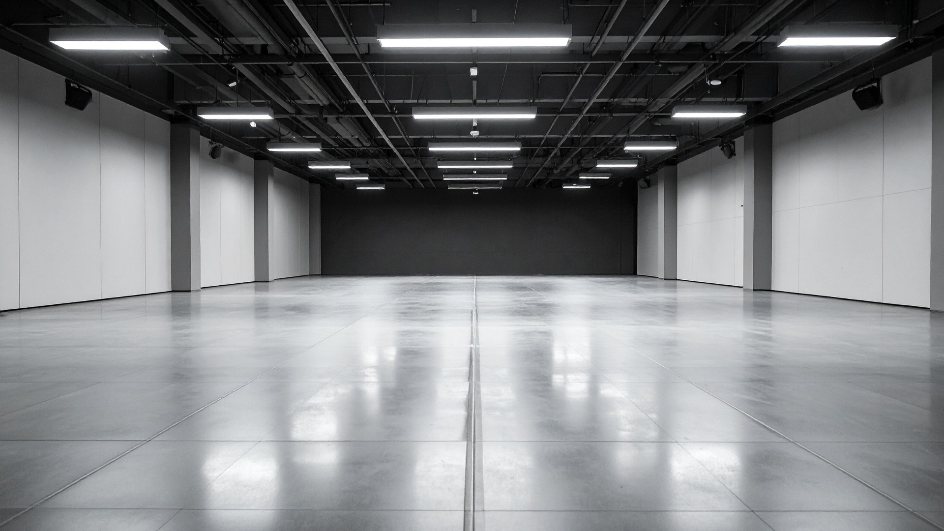 Empty industrial hall, polished concrete floor, overhead lights, dark central wall.
