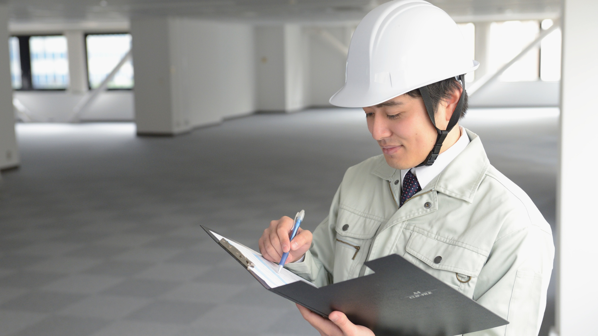 Construction worker in hard hat writing on a clipboard in an empty office space.