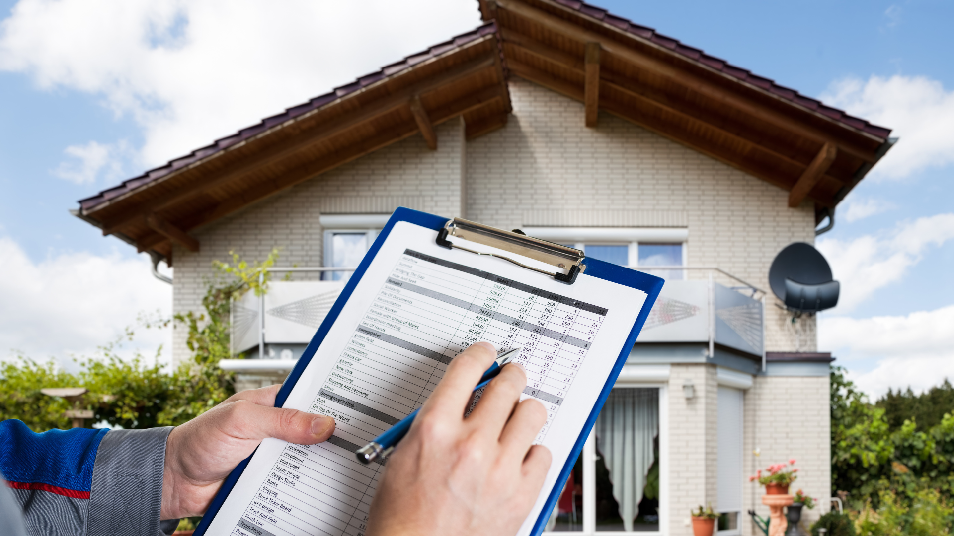 Person holding clipboard, inspecting exterior of a two-story house under a blue sky.