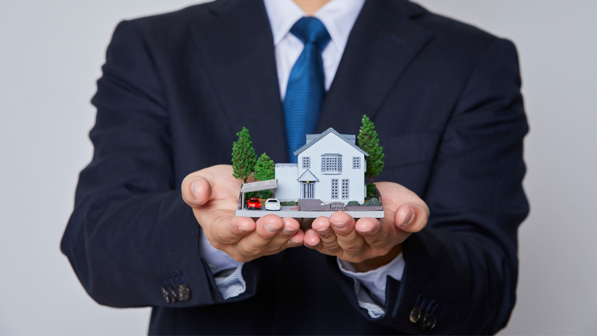 Man in suit holding a model house in outstretched hands.