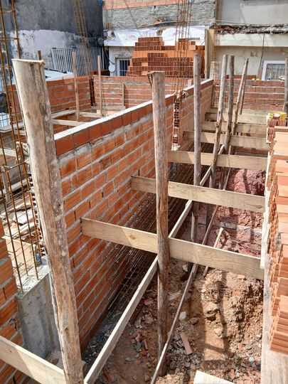 A construction site featuring unfinished brick walls, wooden support beams, and exposed steel rebar.