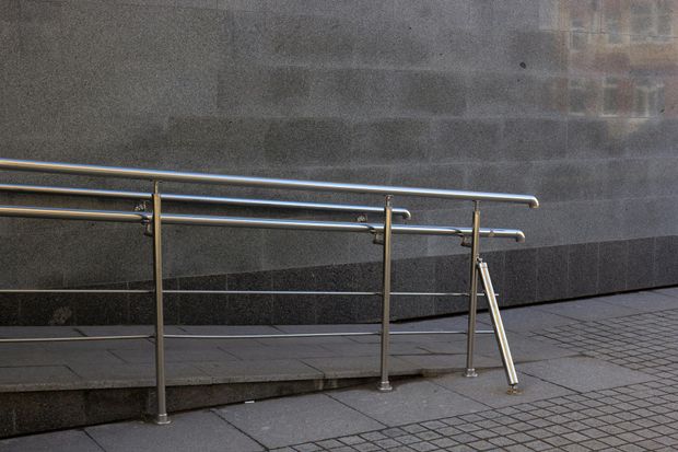 A metal handrail runs along a concrete accessibility ramp next to a textured stone wall.