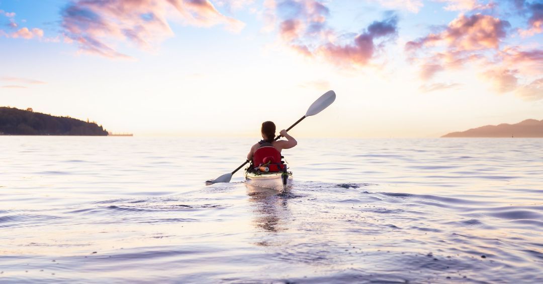 woman kayaking in the ocean with a blue sky and pink clouds
