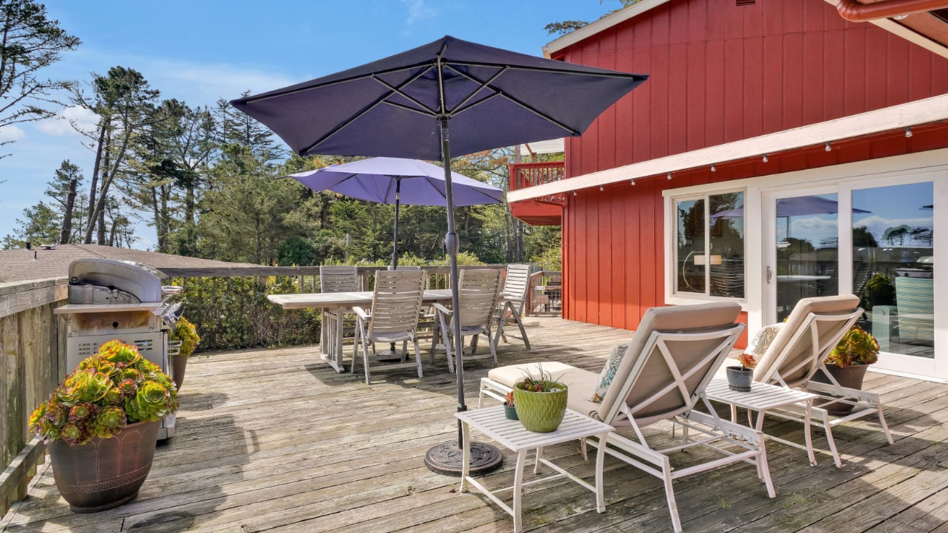 A deck with chairs and umbrellas in front of a red barn