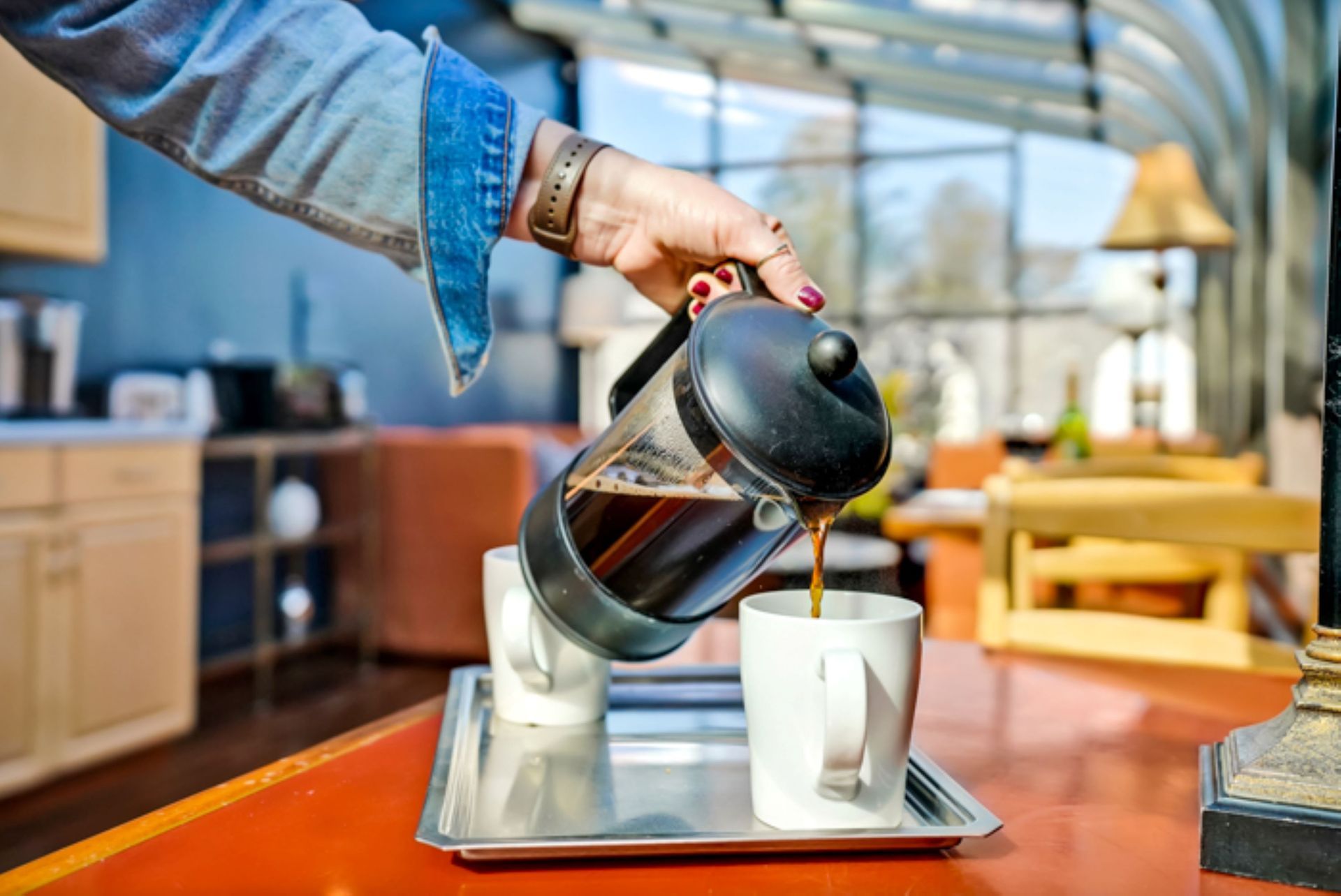A person is pouring coffee from a french press into two cups.