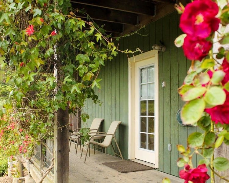 A green house with a porch with chairs and flowers