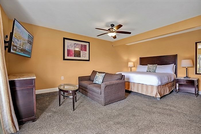 A hotel room with a king size bed , couch , television and ceiling fan.