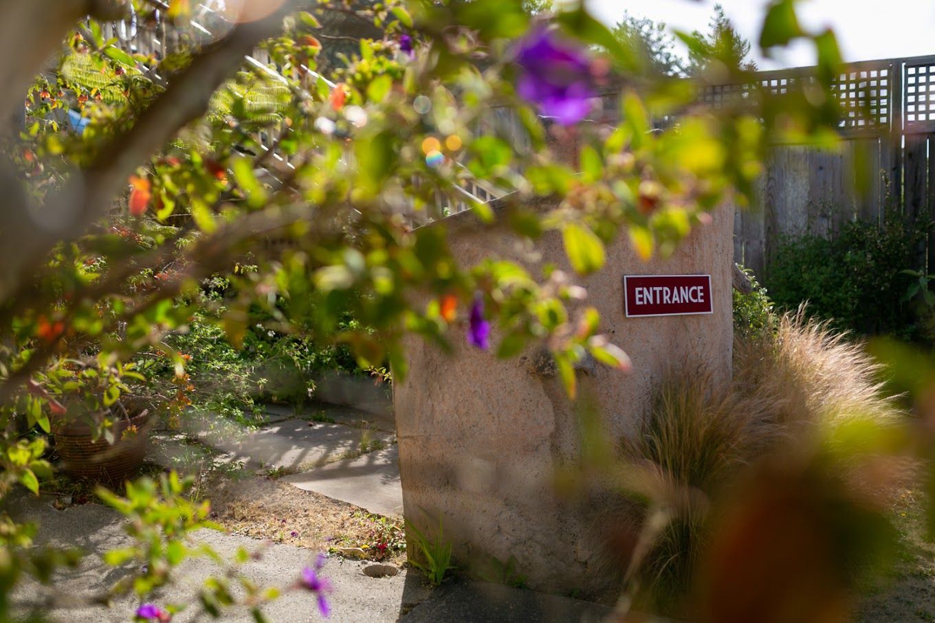A stone wall with a sign on it is surrounded by trees and bushes.