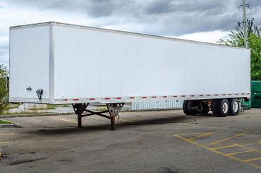 View of a white parked transport trailer on a parking lot under a gray sky