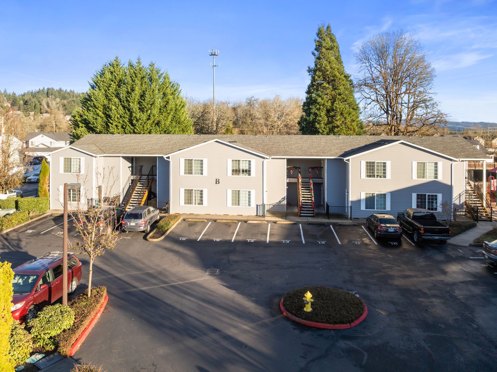 Exterior view of a two-story apartment building with parking and a small landscaped area in front.