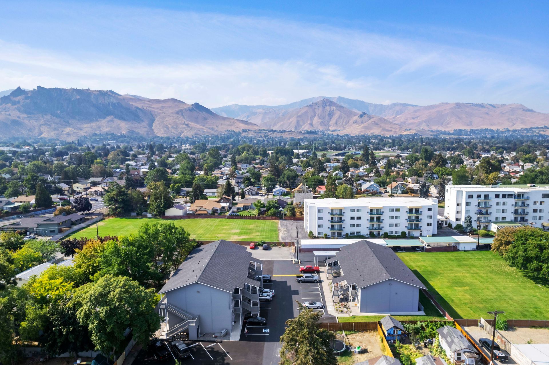 Aerial view of apartment buildings and a town with mountains in the background under a blue sky.