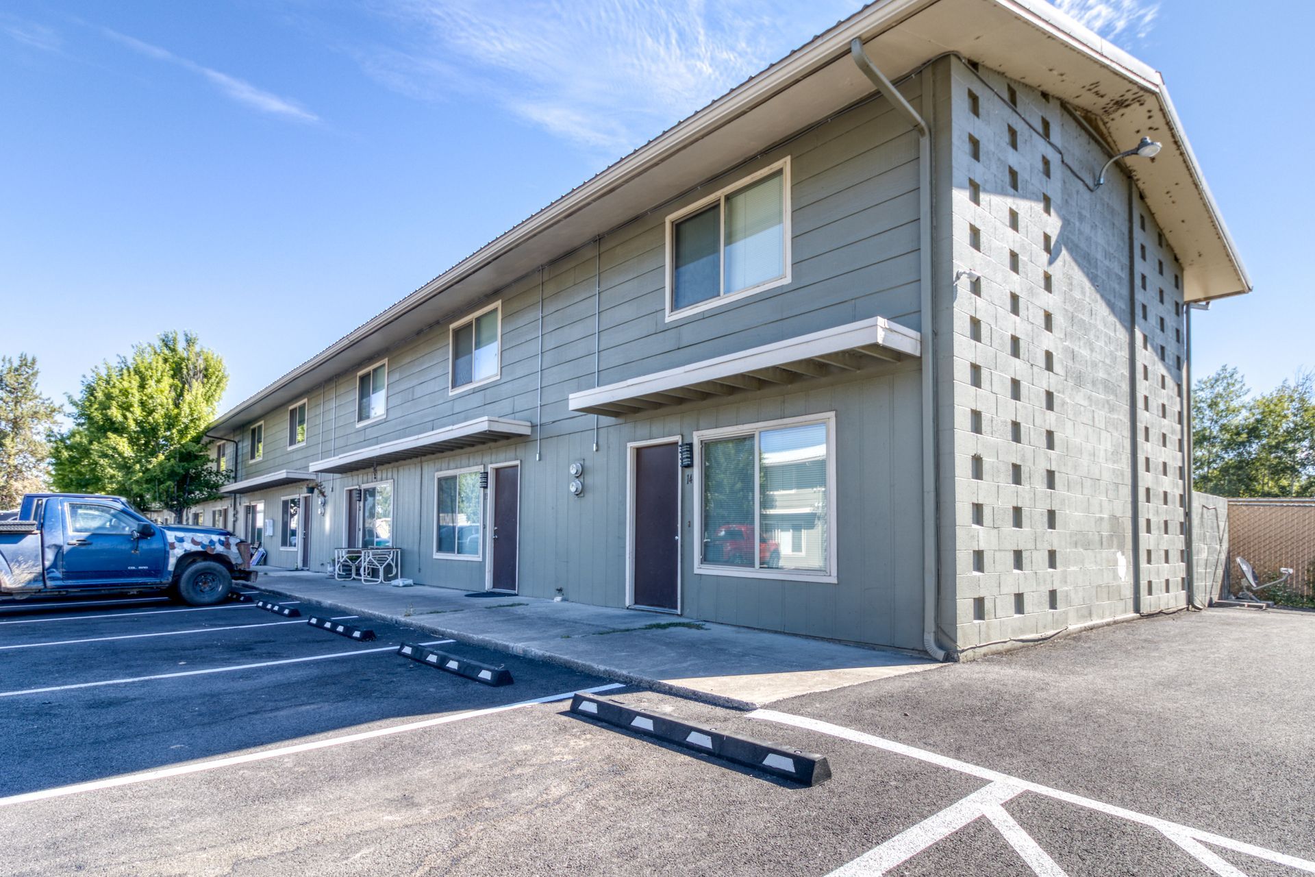 Two-story apartment building with dark gray siding, blue sky, and parking lot in front.