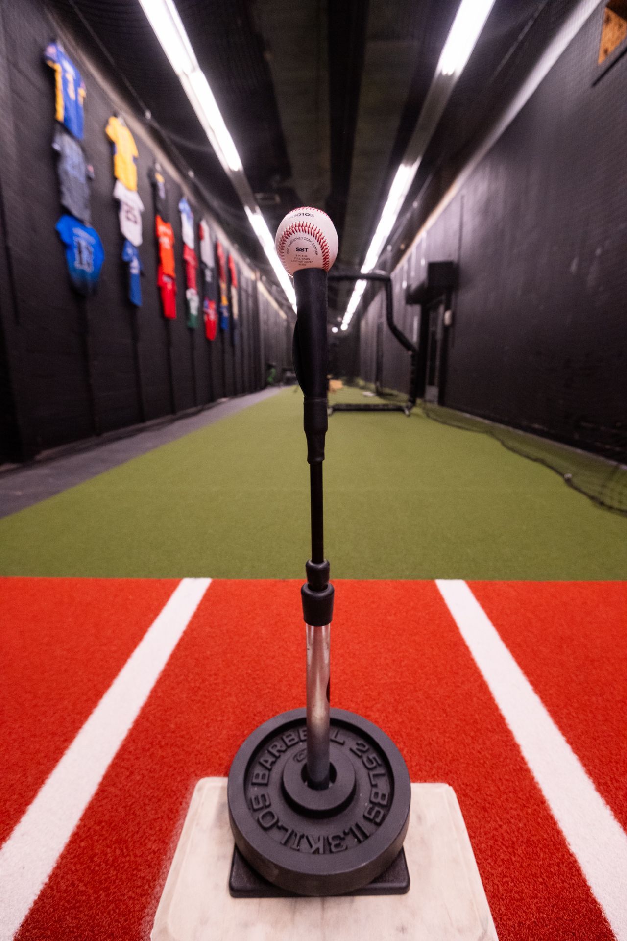 A baseball is sitting on top of a tee in a gym.