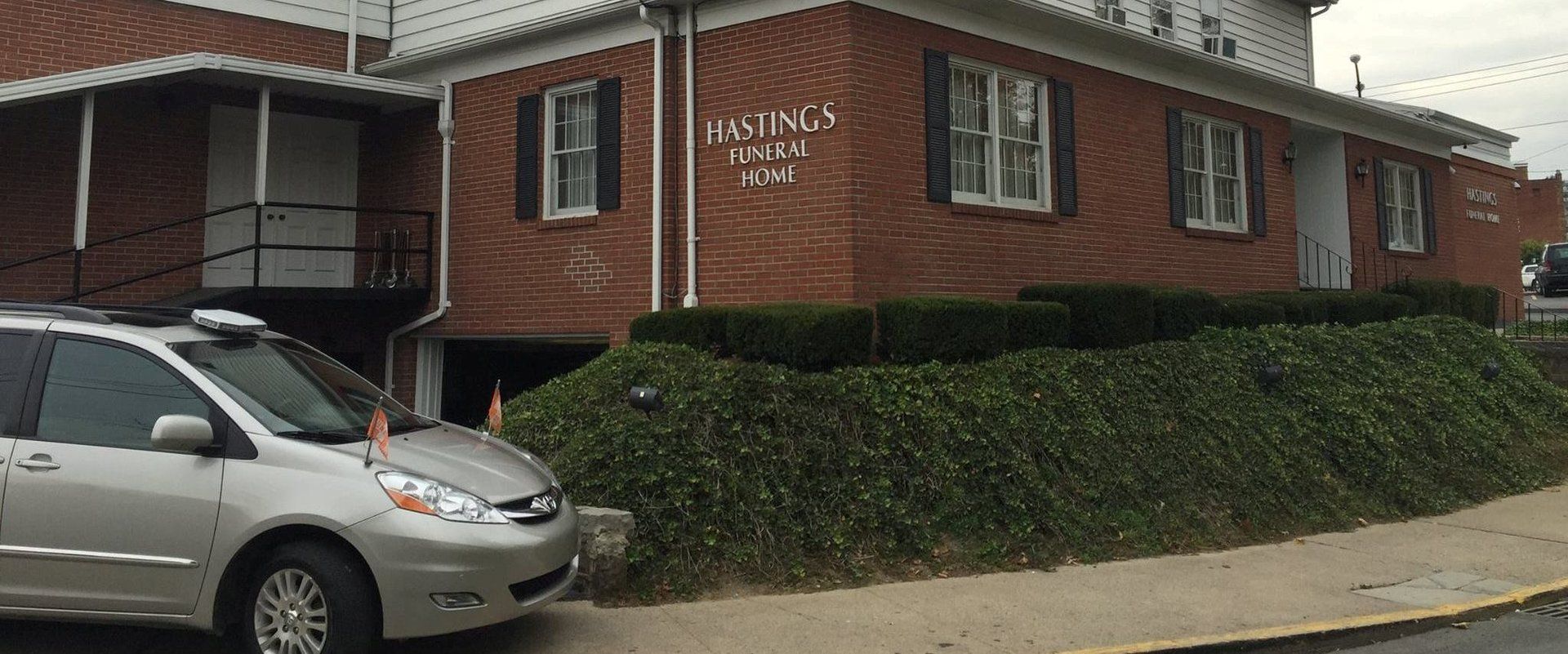 A silver minivan is parked in front of a brick building.