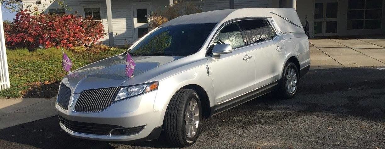 A white funeral car is parked in front of a house.