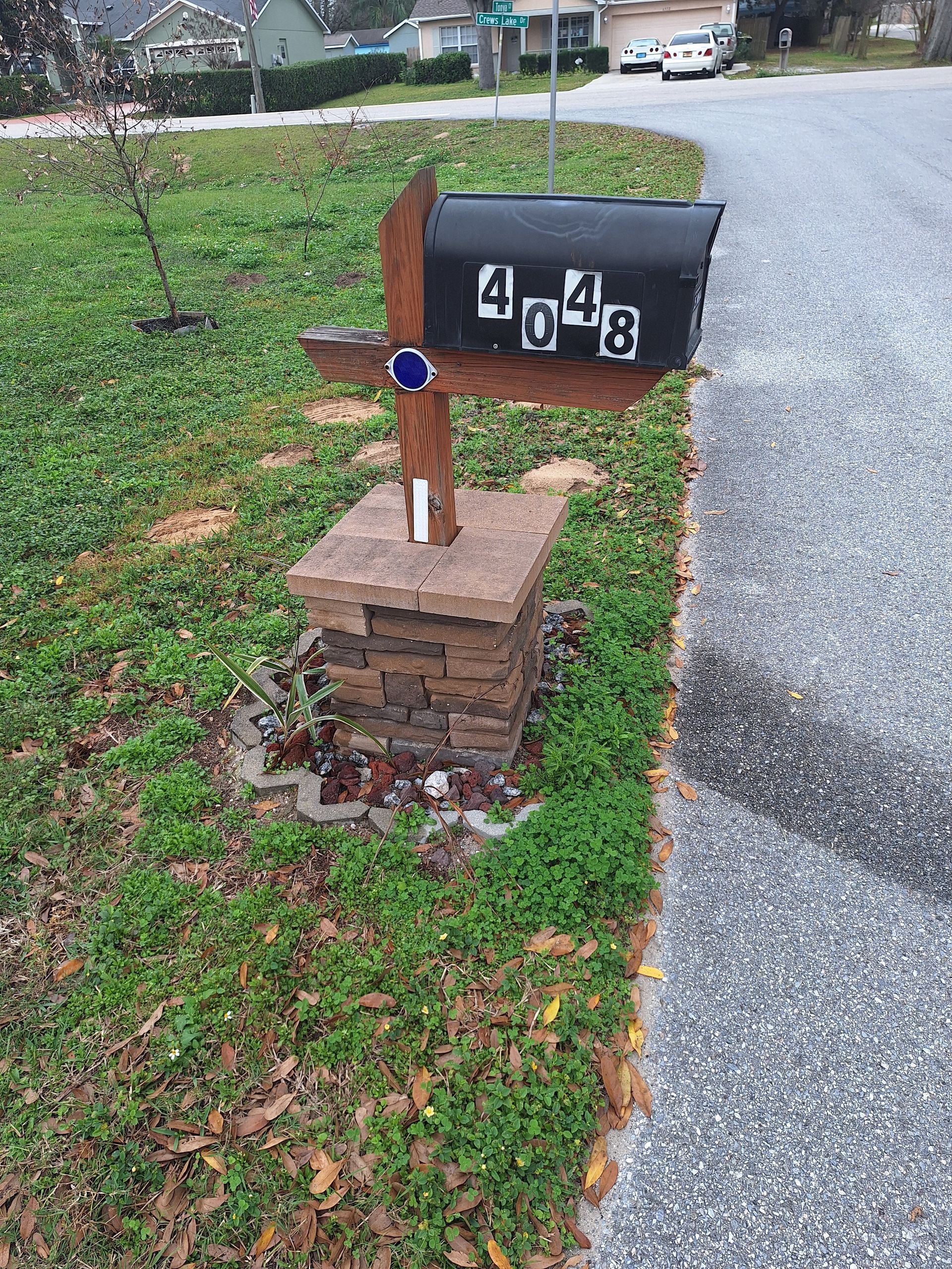 A black mailbox is sitting on a stone pillar next to a gravel road.