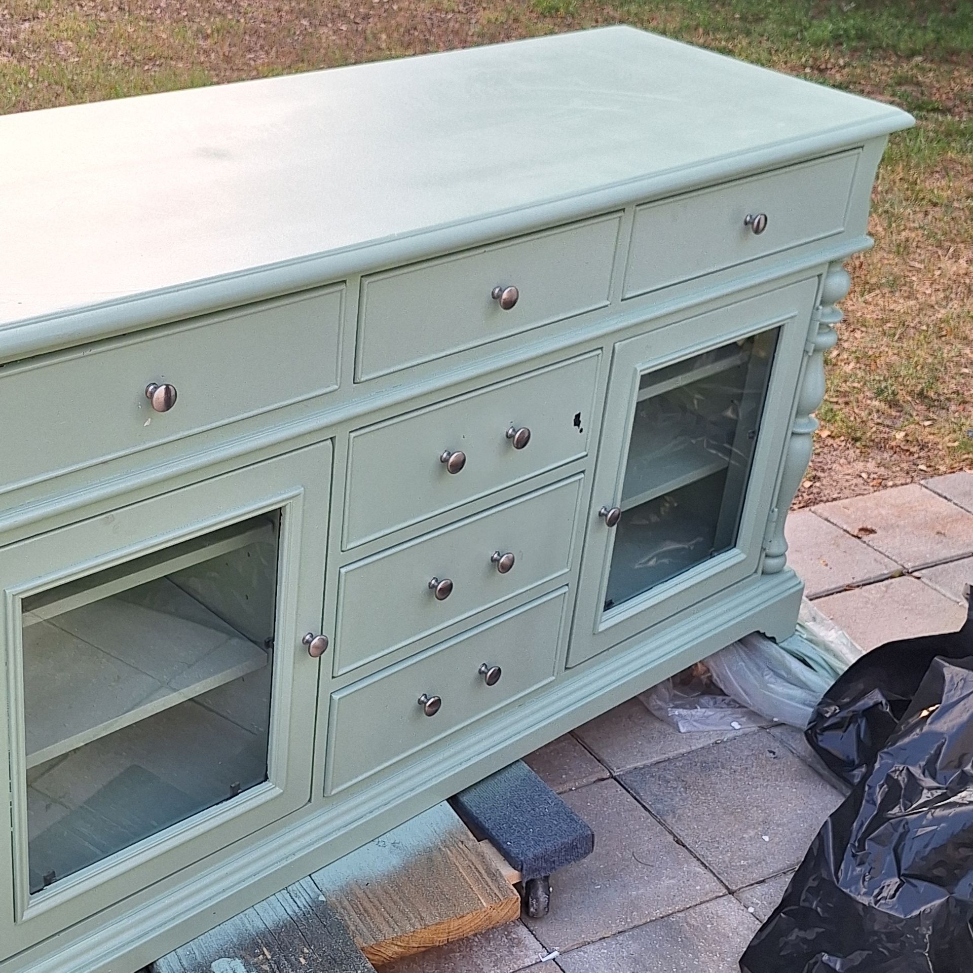 A green dresser with drawers and glass doors is sitting on a sidewalk.
