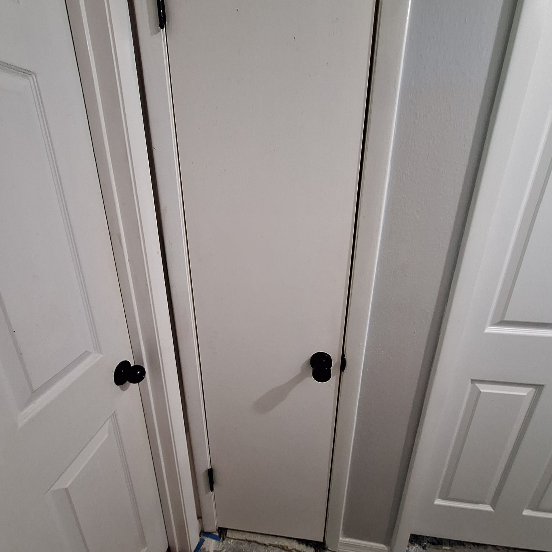 A closet with white doors and black knobs