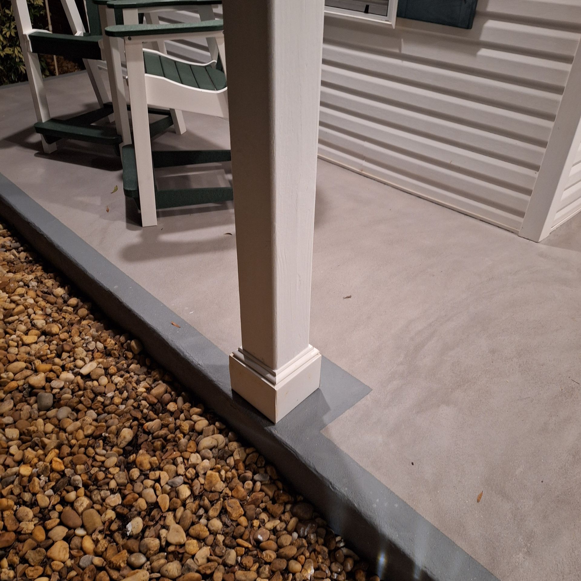 A porch with a white post and green chairs