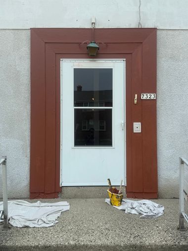 White door with window in a brown wall, lit by a lamp, with a yellow can and white cloths on the ground.