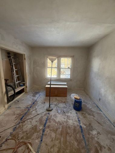 Small unfinished room with a window, bare walls and floor, and a few construction materials inside.