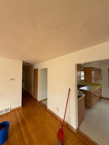 Empty apartment hallway with wooden floor, cream walls, and a red broom near a kitchen doorway