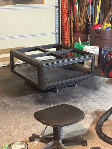 Garage workshop with a black metal cart, small stool, and tools along the wall.