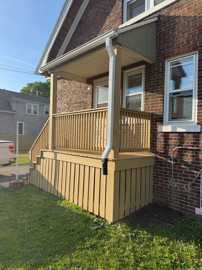 Wooden porch ramp and railing attached to a brick house on a sunny day