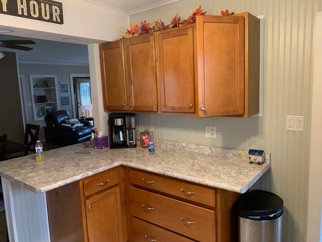 Small kitchen corner with wood cabinets, speckled countertop, coffee maker, and black trash can.