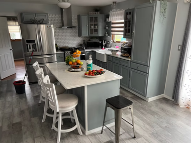 Bright gray kitchen with island, white stools, stainless fridge, and a fruit centerpiece.