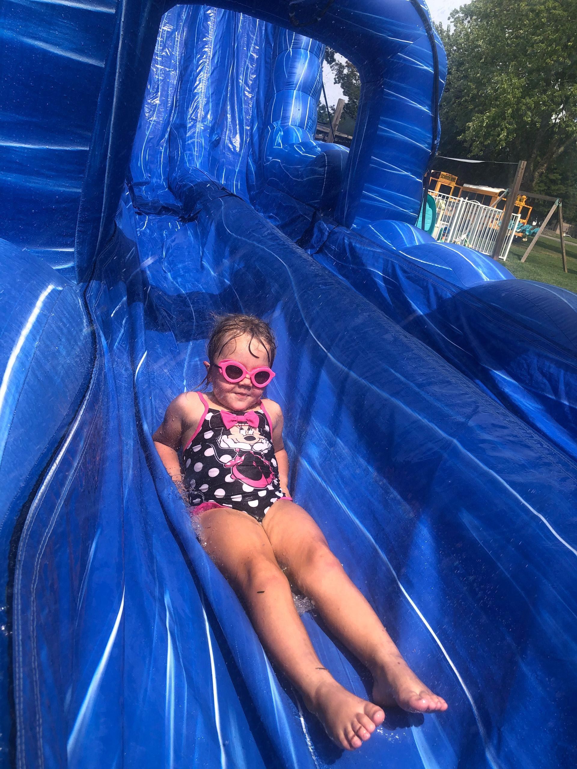 A little girl is sitting on top of an inflatable water slide.